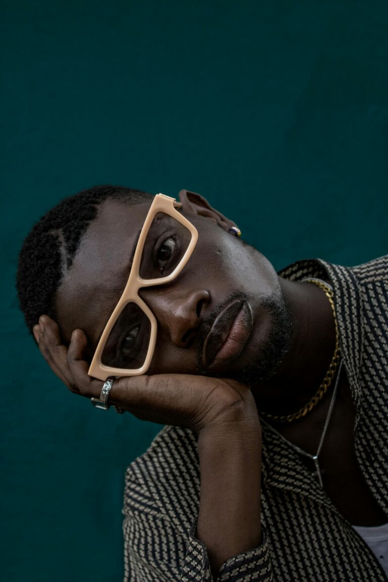 A thoughtful pose by a stylish man in a Nigerian studio shoot, wearing glasses.