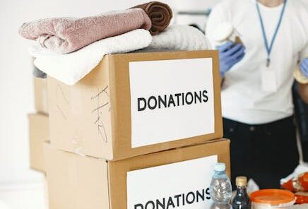 A volunteer organizing donation boxes filled with clothes and essential supplies indoors.